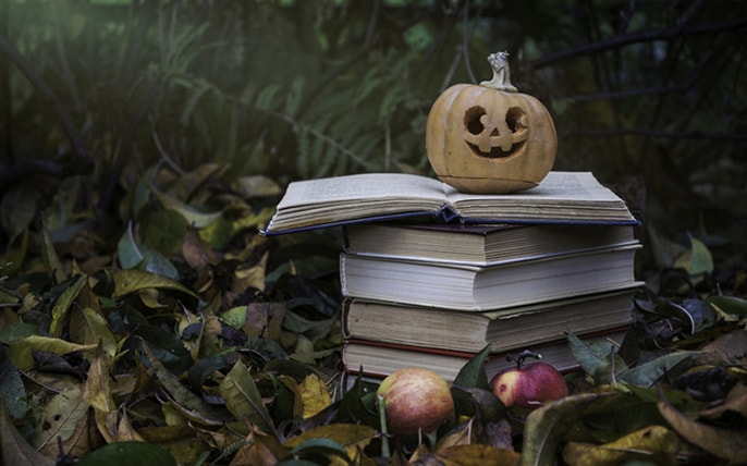 A pumpkin sits atop a stack of books in the forest