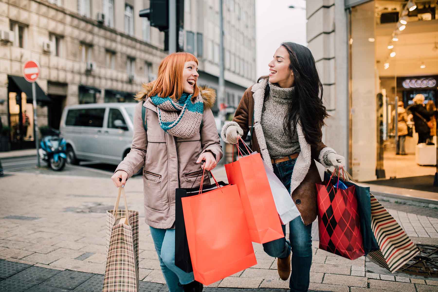 Two happy women holding shopping bags in the city.