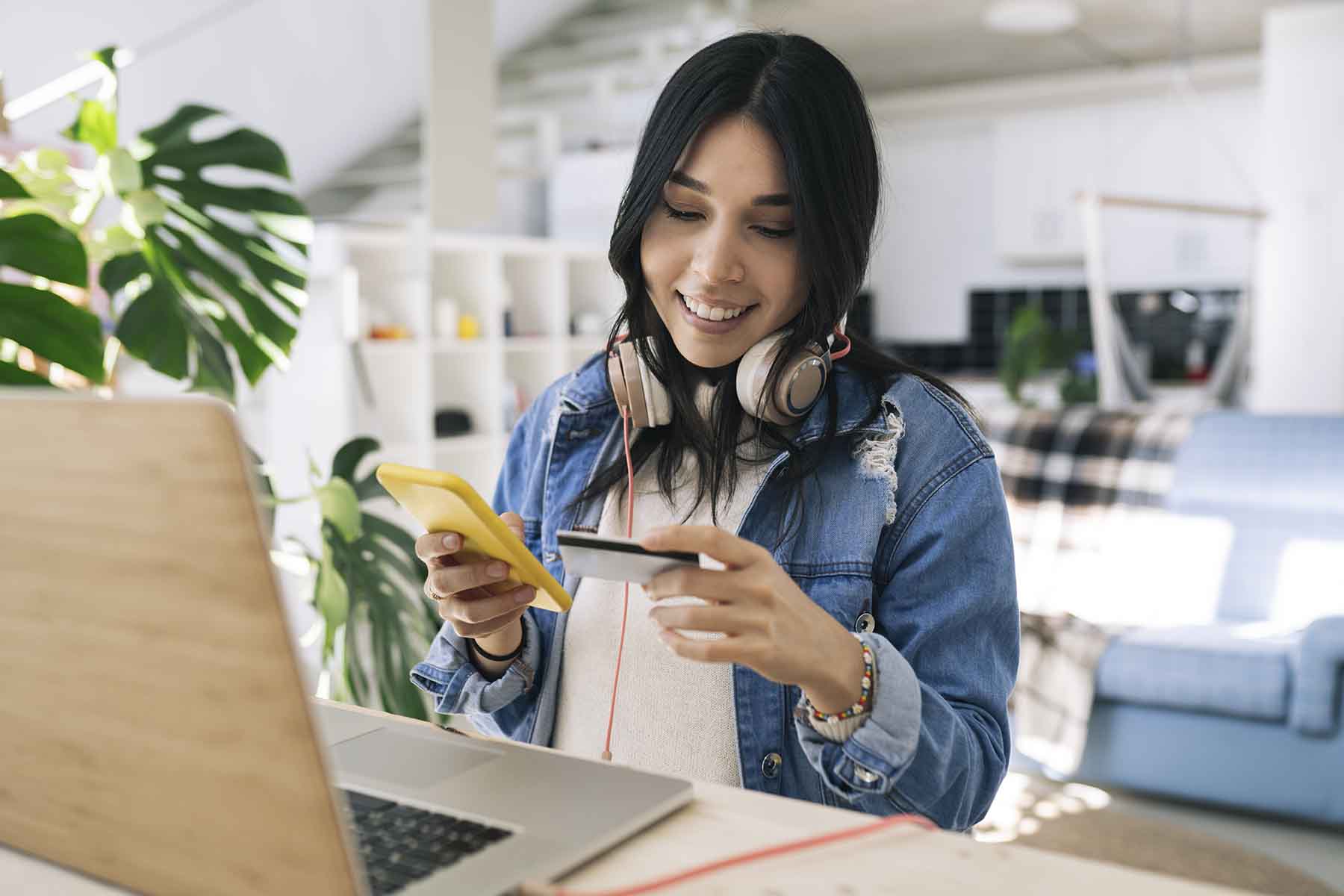 Woman with headphones uses credit card to make a purchase on her cell phone