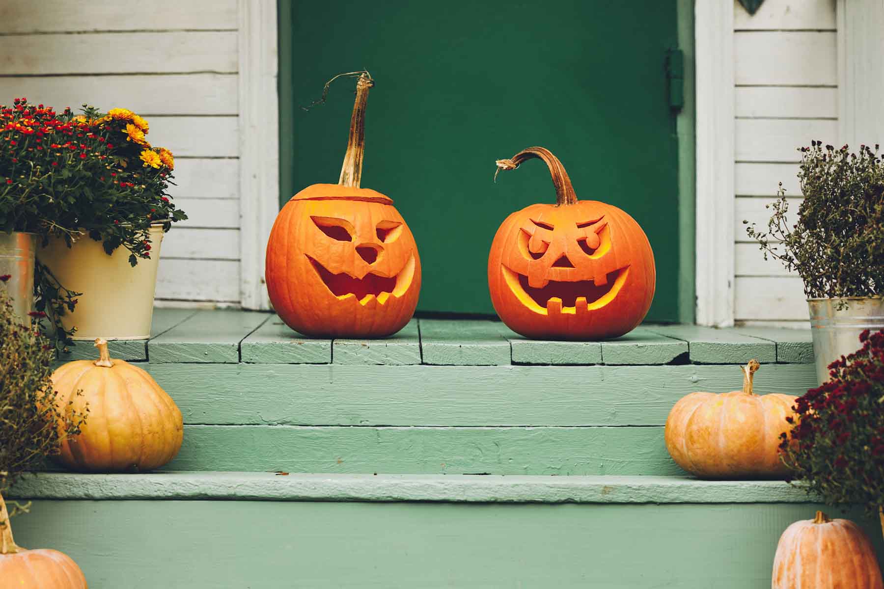 A rustic porch with carved pumpkins and mums.