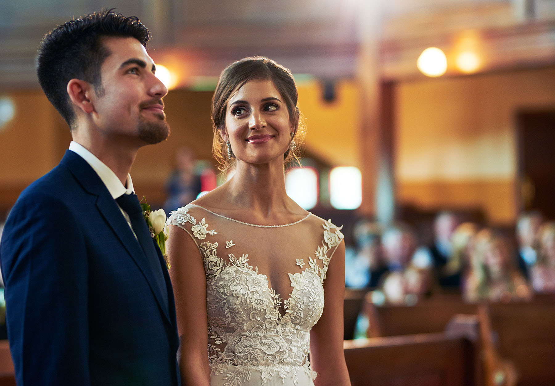 Smiling bride and groom stand side by side in front of congregation.