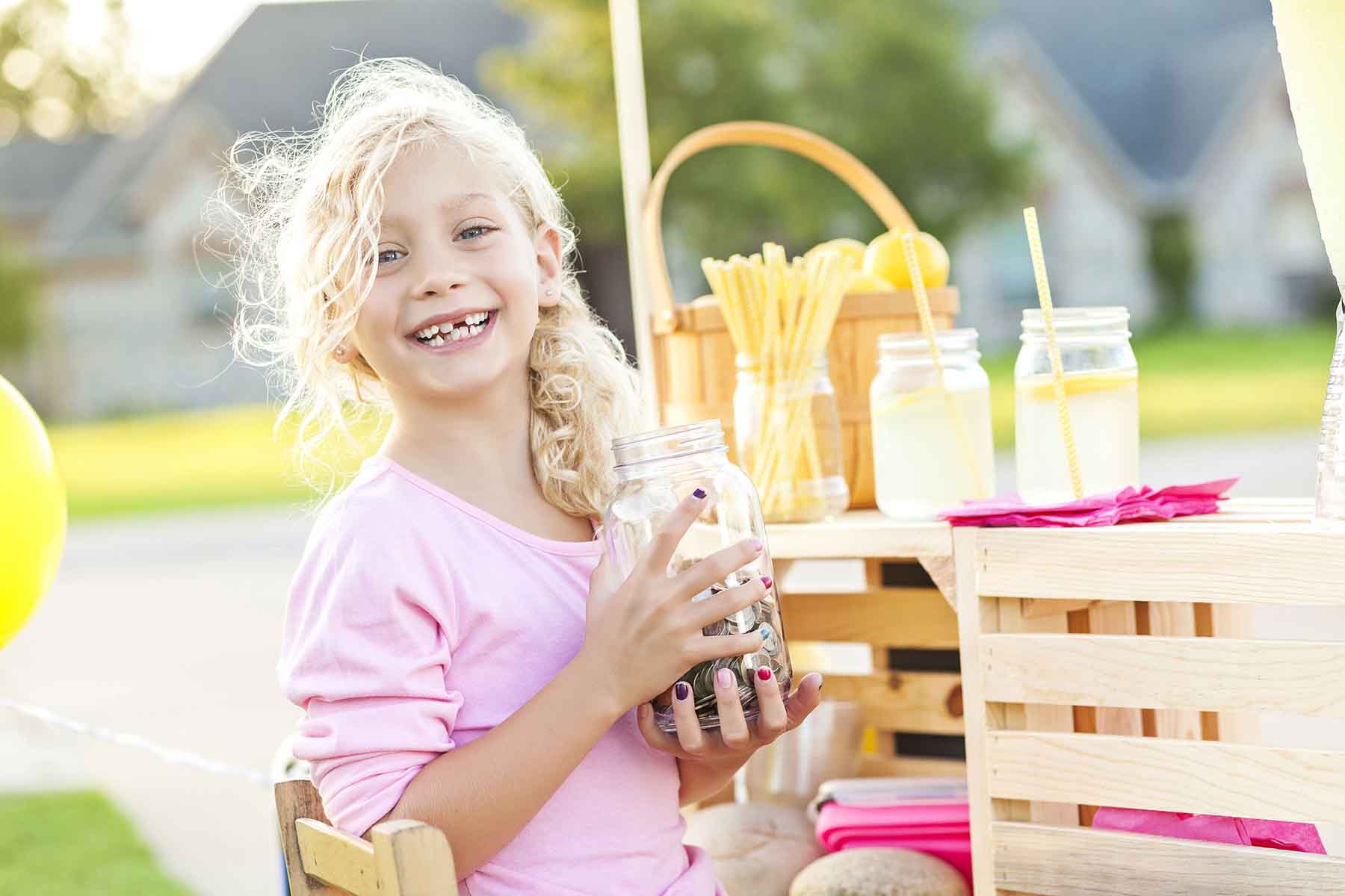 Young girl smiling with a jar full of coins she earned from working her lemonade stand