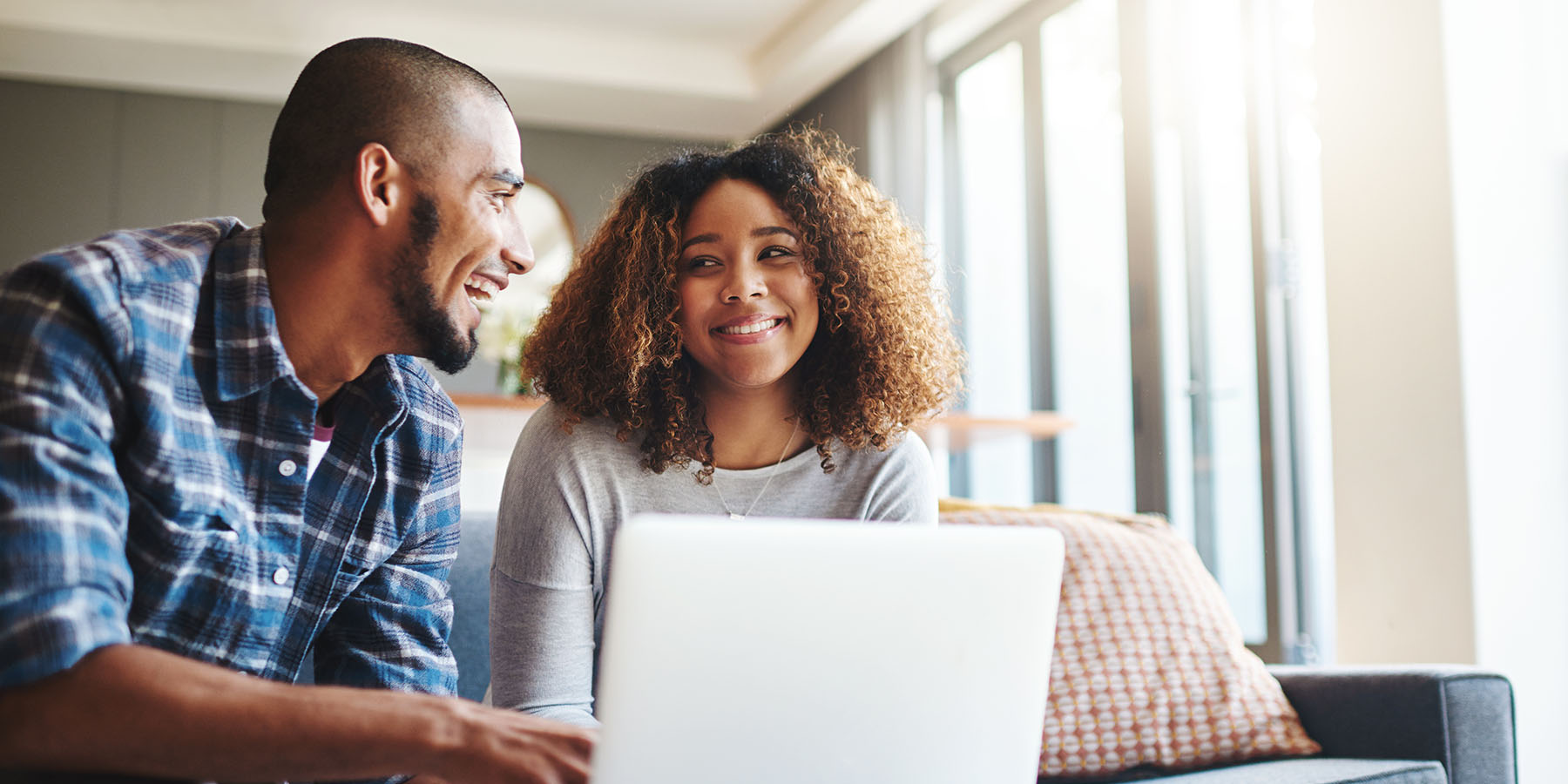 A smiling couple sitting in their living room with a laptop discussing finances
