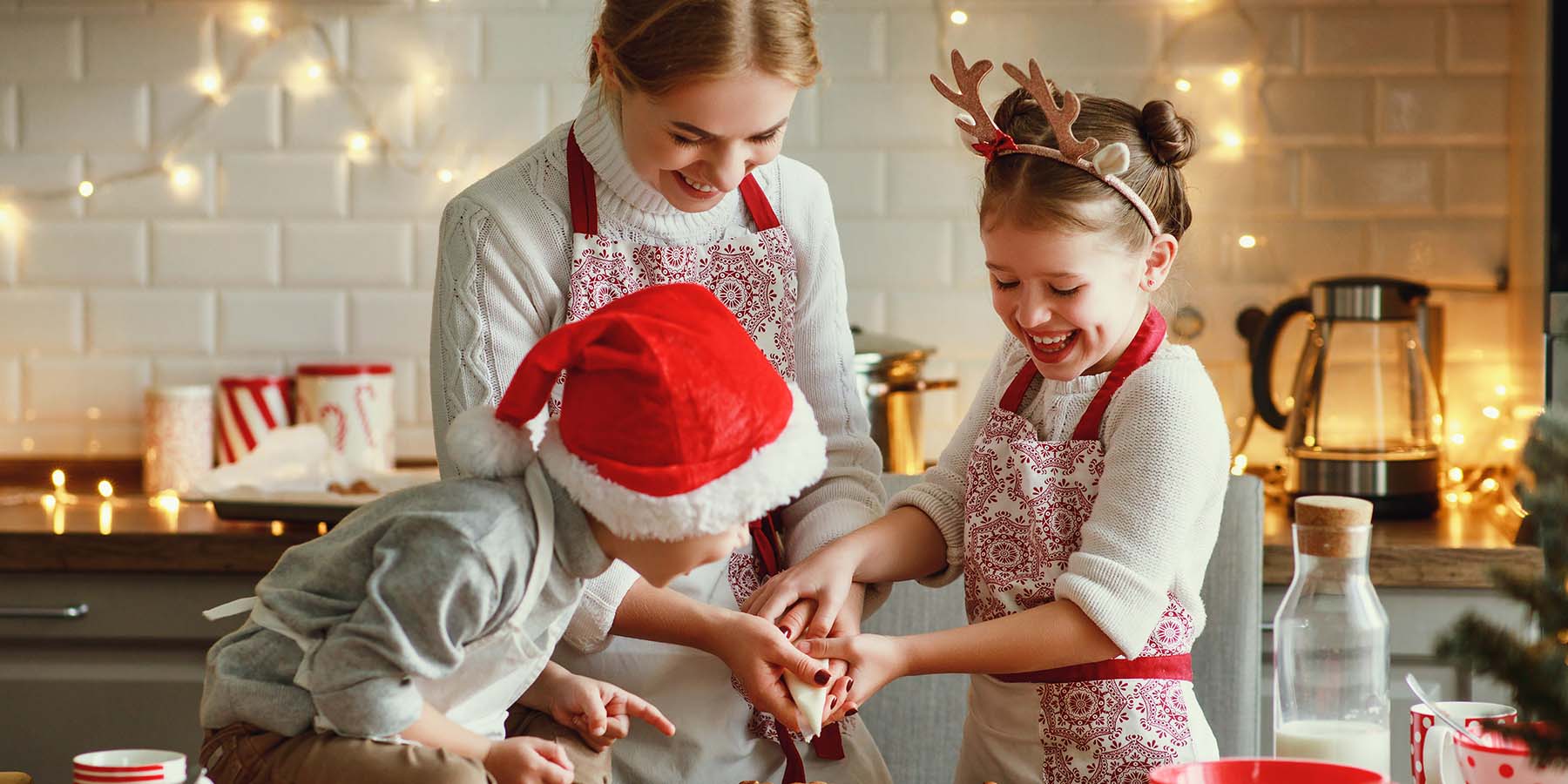 A young mother decorates cookies for the holidays in her kitchen with her two young children