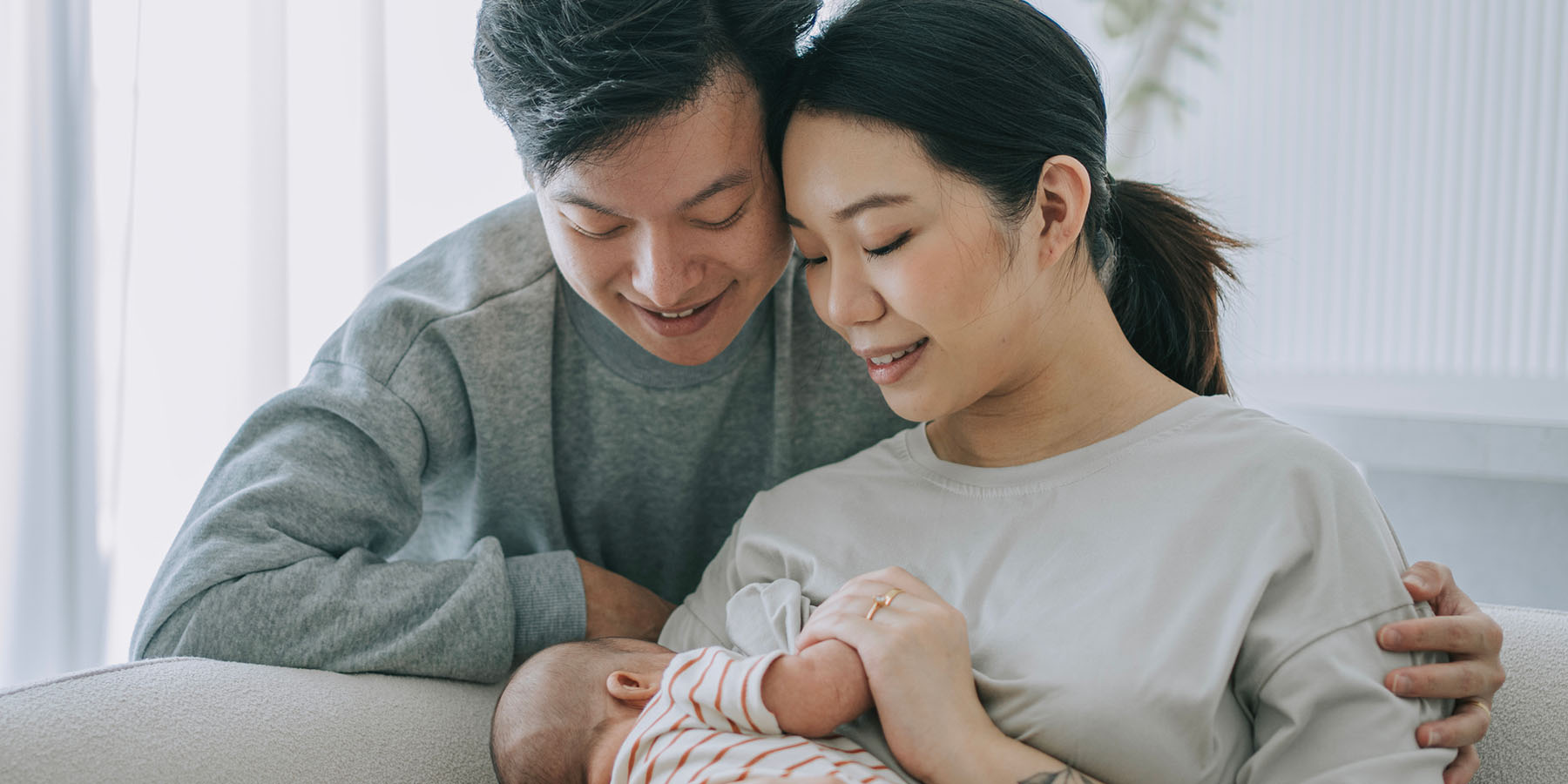 A smiling couple looks down at their newborn baby, who is in the mother's arms