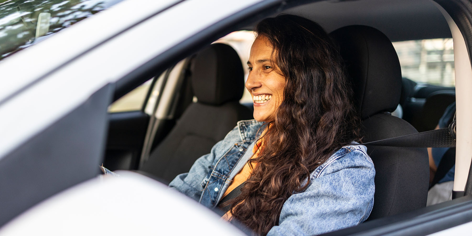 A young woman smiling, sitting in the driver's seat of her car