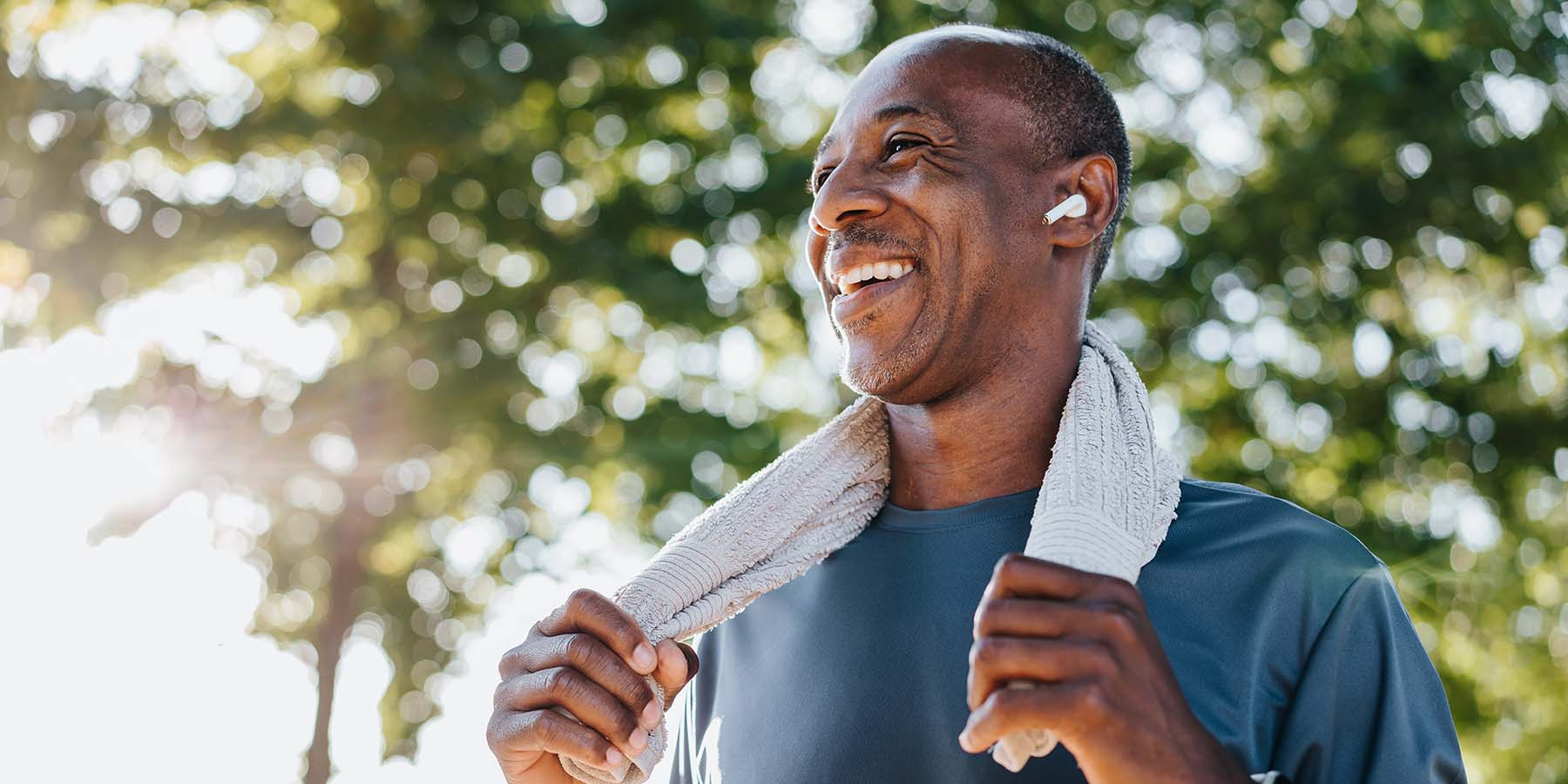 A man stands in the sun holding a towel after exercising