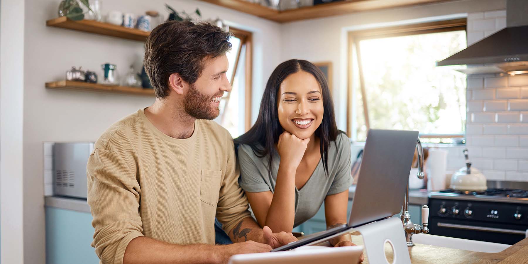 A young couple sitting in their kitchen looking at a laptop, managing finances