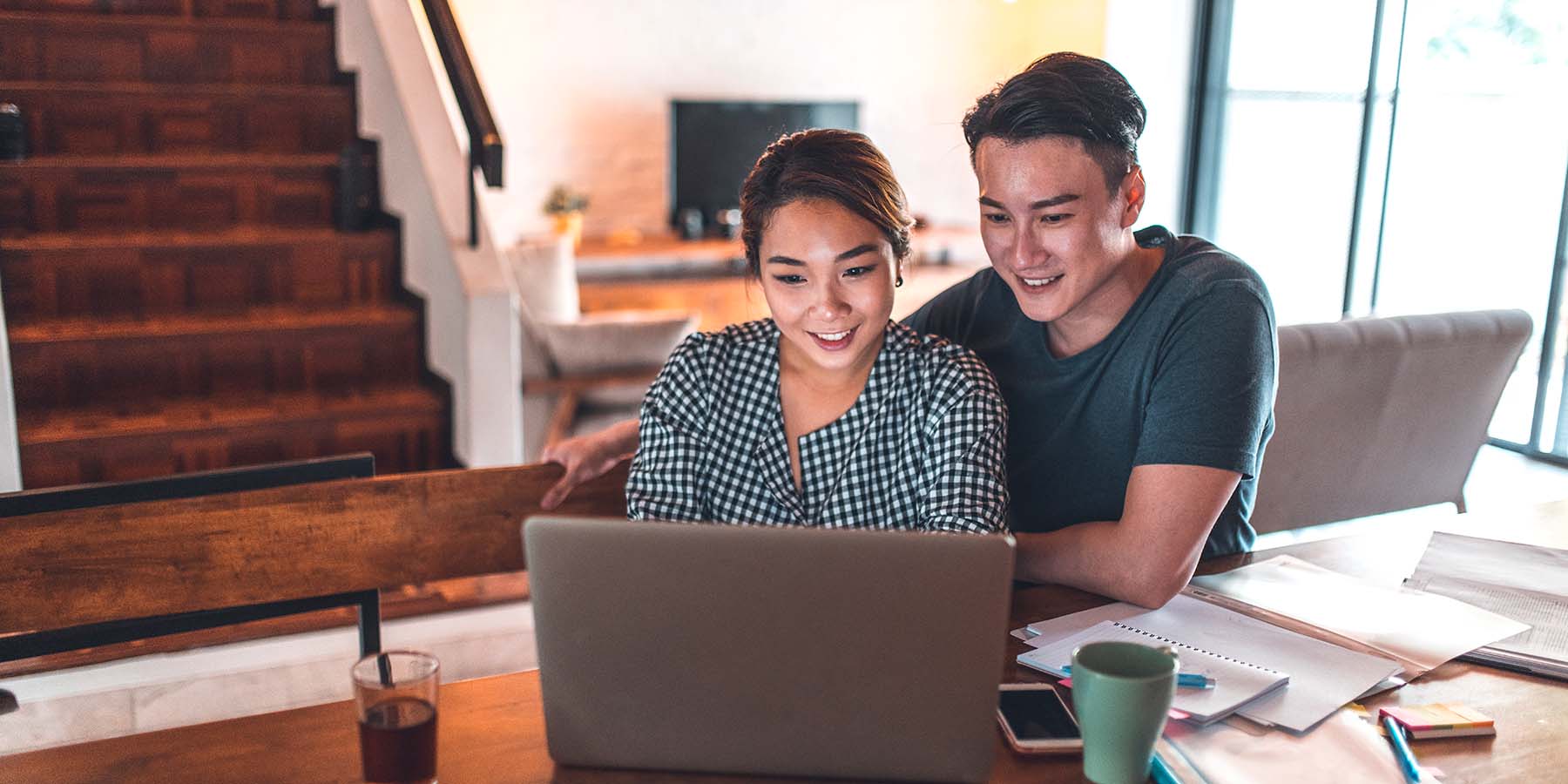 A couple sits at a table in their home in front of a laptop