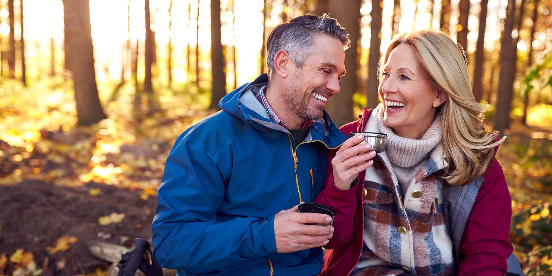 A smiling couple sits together in the woods