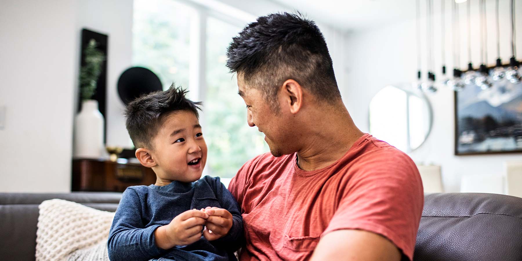 A young father sits on the couch holding his smiling son