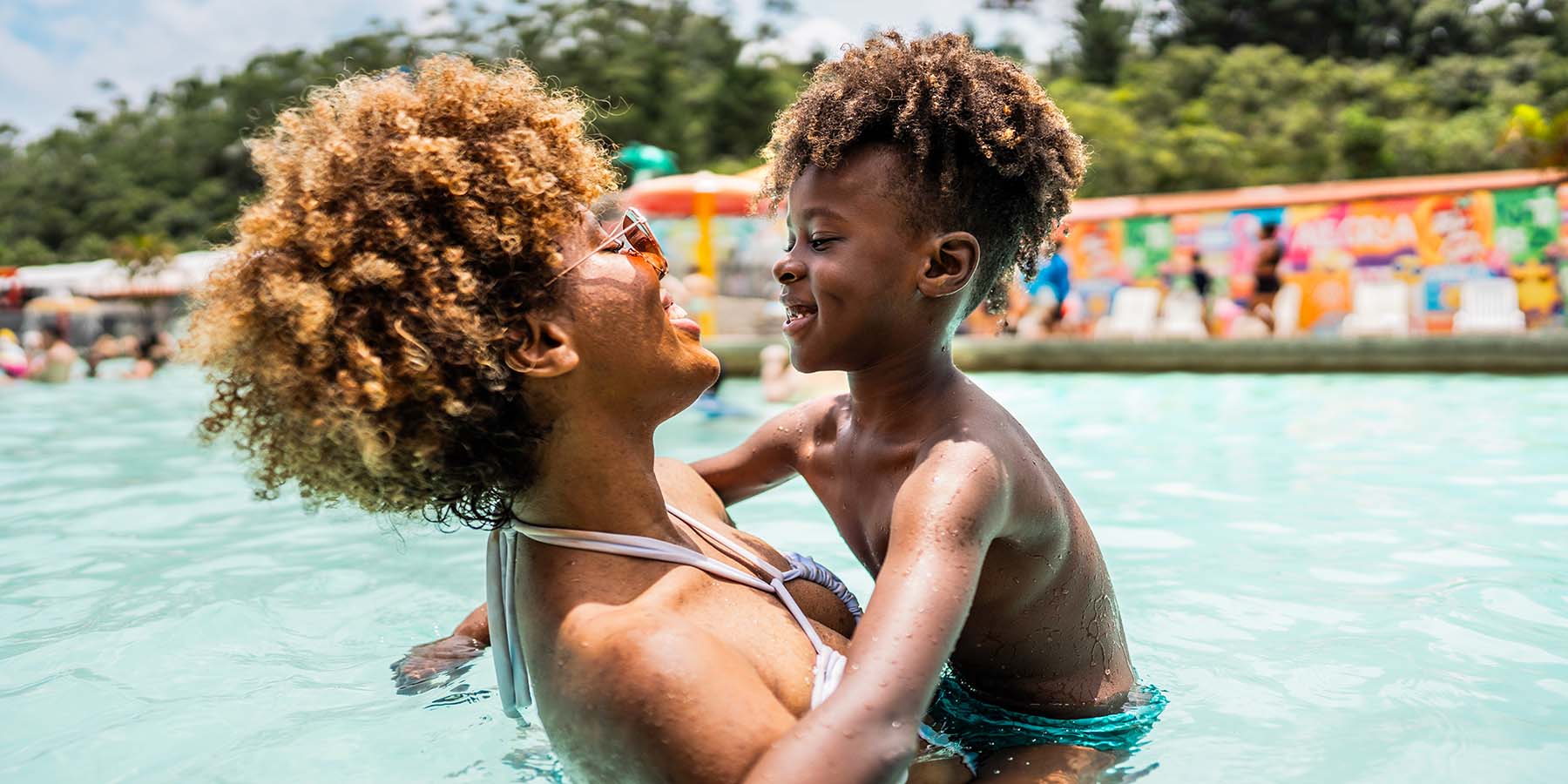 A mother smiles and holds her smiling son in the pool of a vacation resort