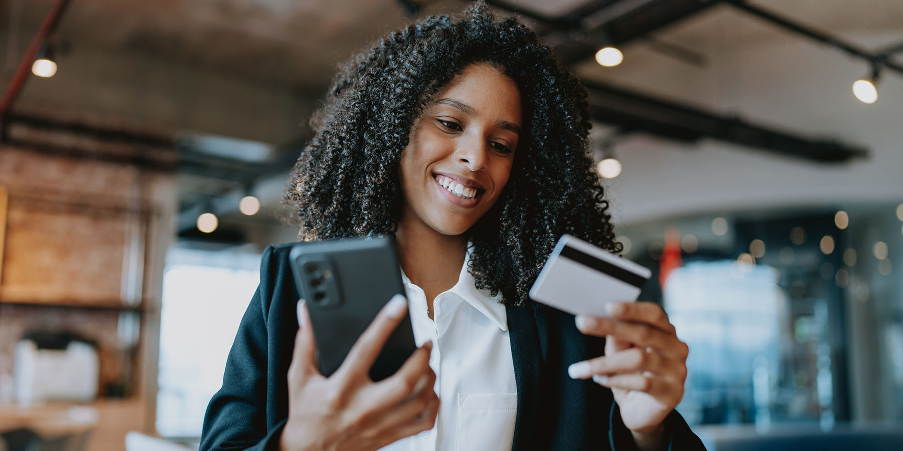 A smiling woman, holding her phone in one hand and her credit card in the other