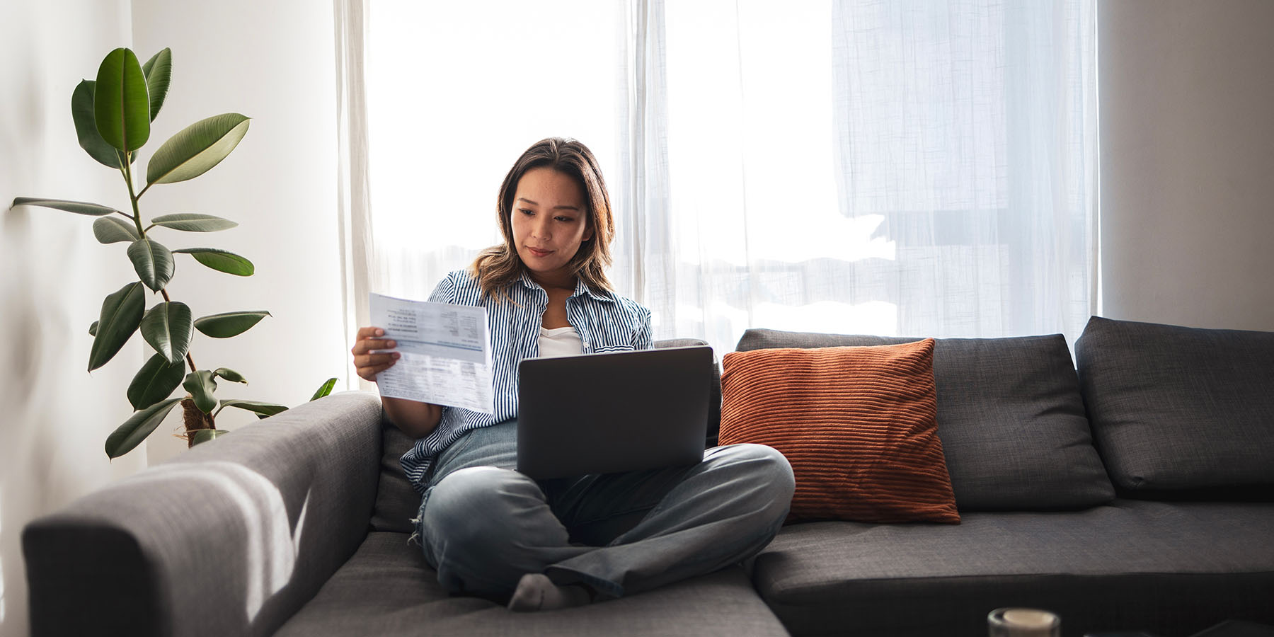 A young woman sits on her sofa with her laptop, reviewing a document