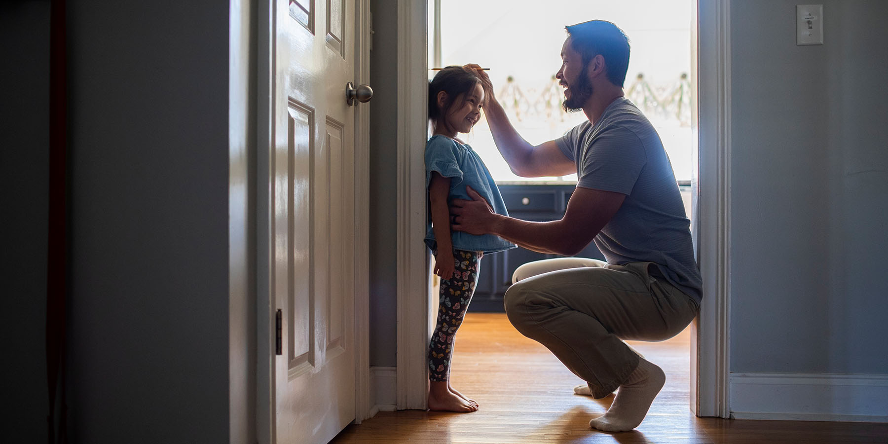 A father crouches down and measures his young daughter's height against a door frame