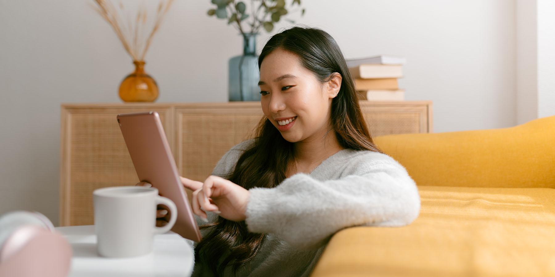 A young woman sits in her living room, using a mobile tablet