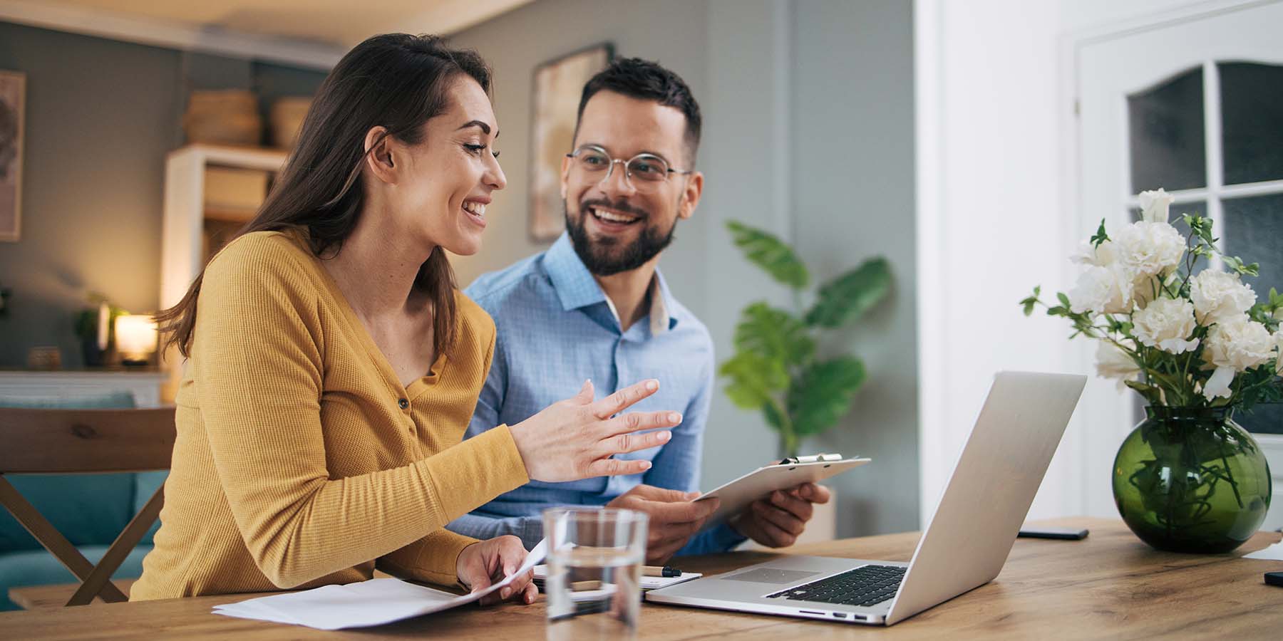 A young couple sitting at their dining room table with a laptop, reviewing finances