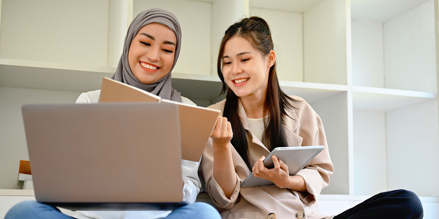 Two young women sitting with a laptop and tablet, working on schoolwork