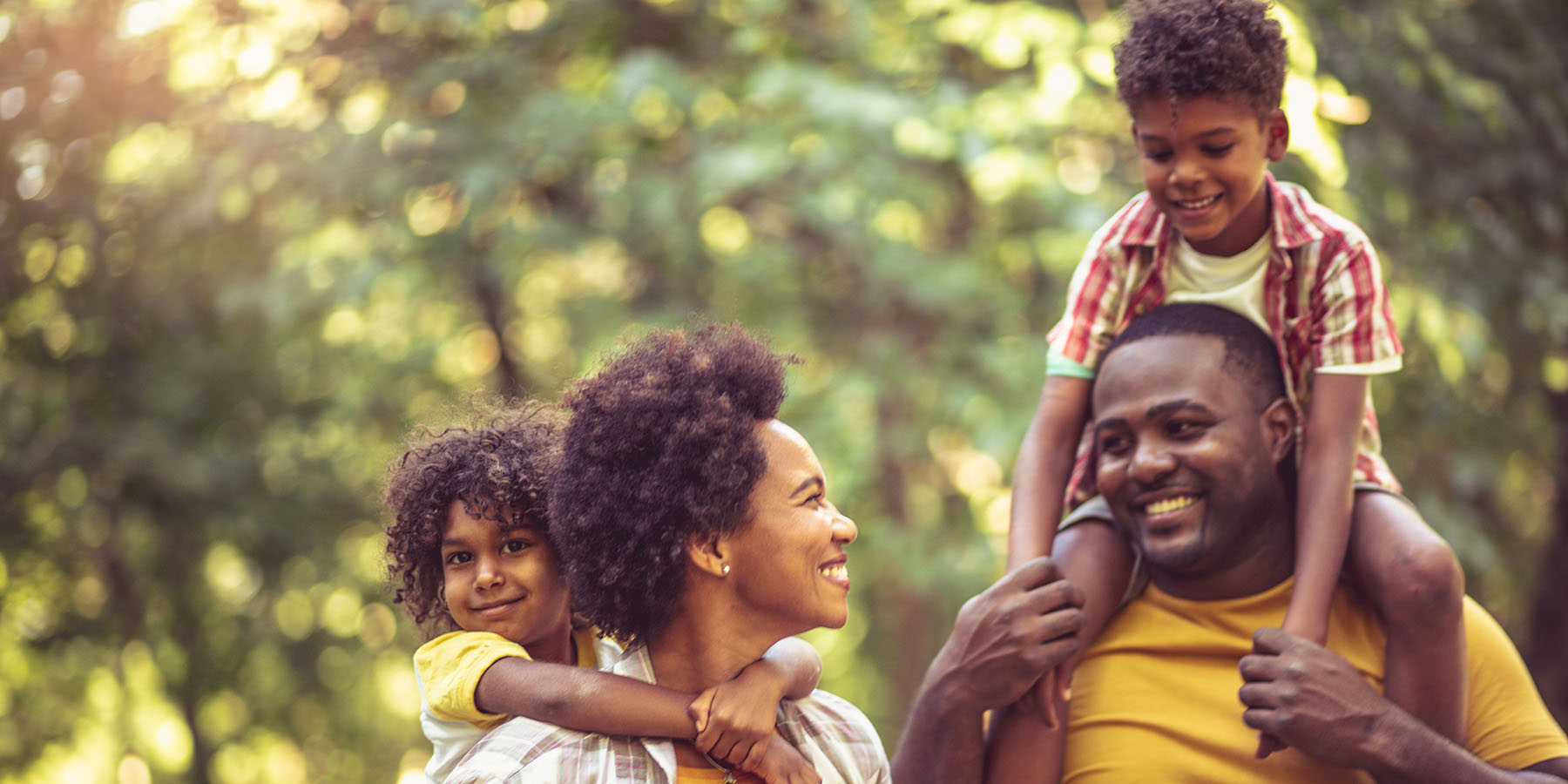 A young family walking in nature, with the children on the parents' shoulders
