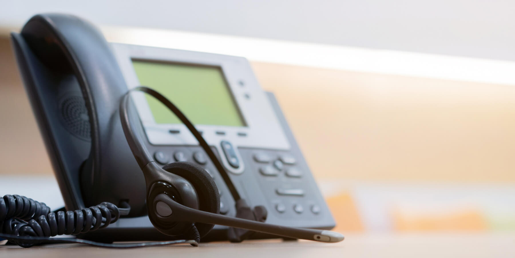 A call center phone and headset sit on a desk