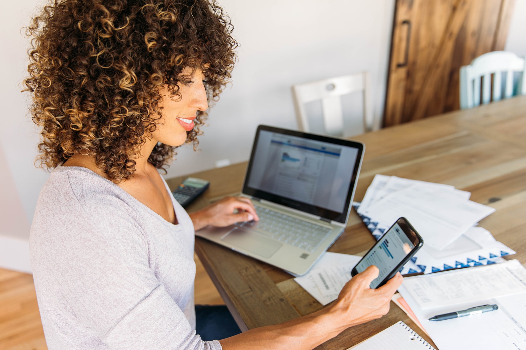 A woman uses her laptop and smartphone to create her budget