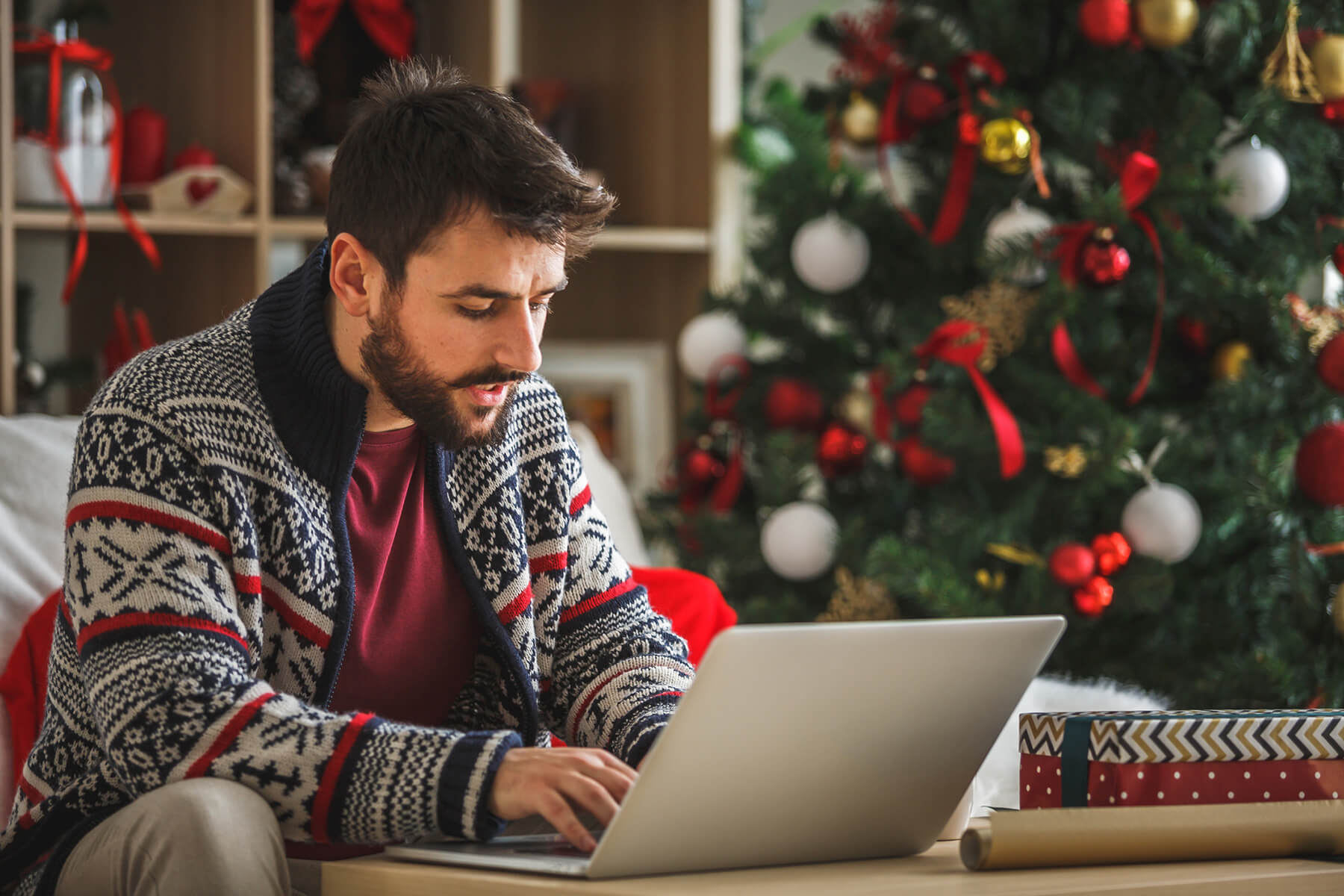 Man sits with a laptop in his living room, decorated for the holidays