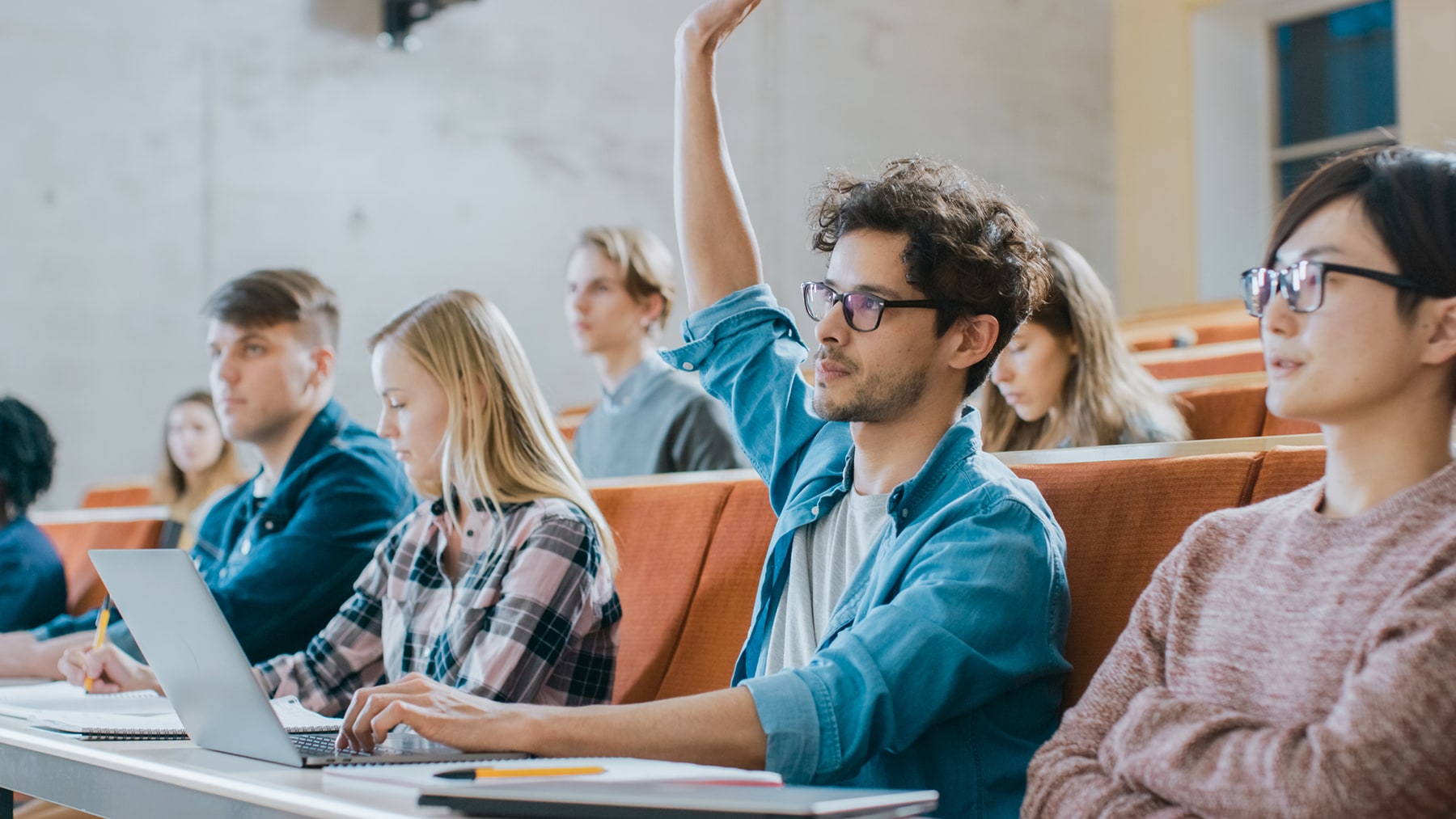 Student raising his hand in a college auditorium