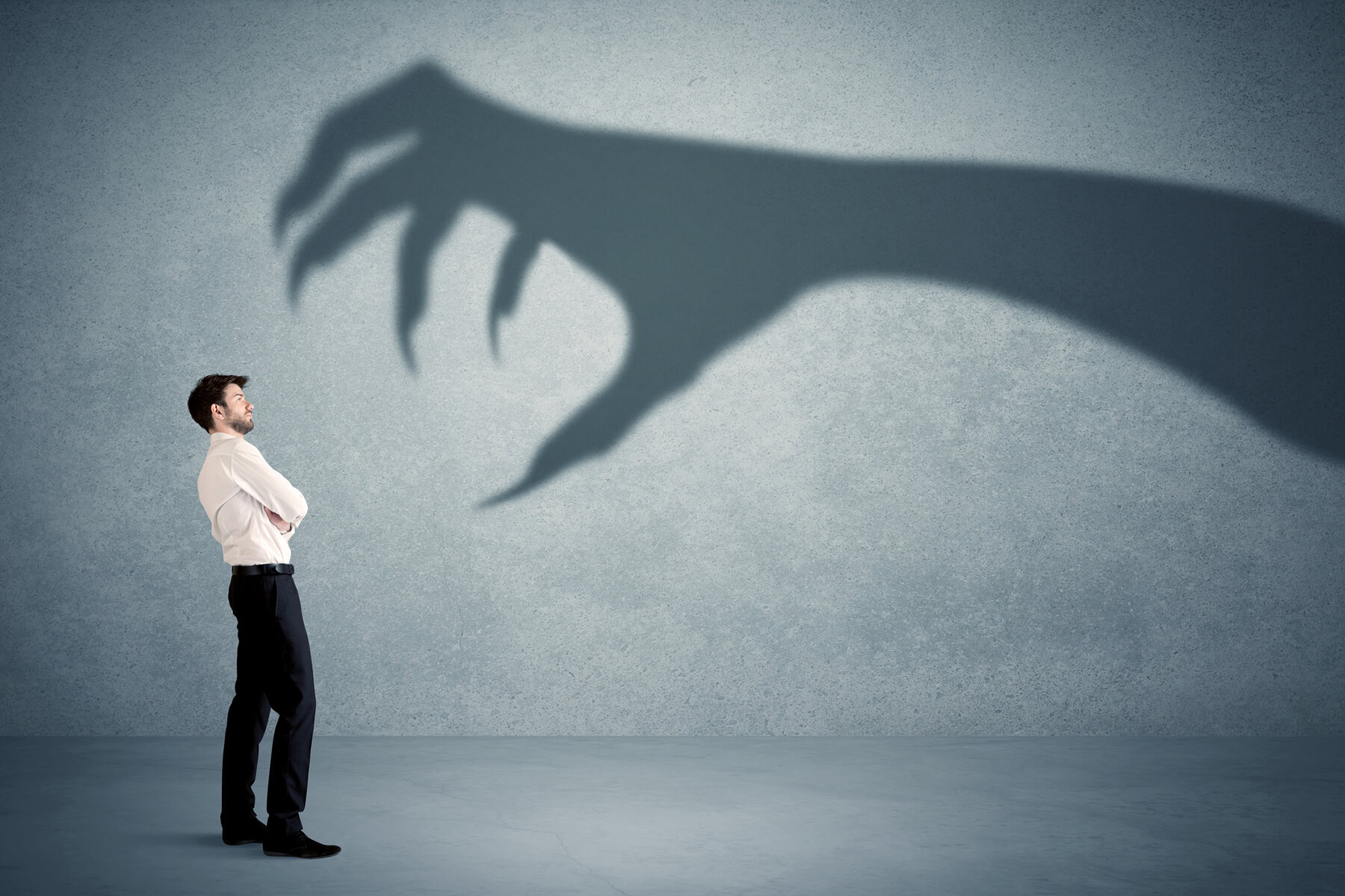 Businessman stands facing the shadow of a monster hand
