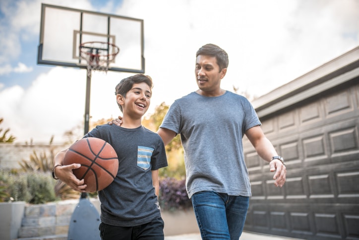 man and boy walking with basketball with hoop in background
