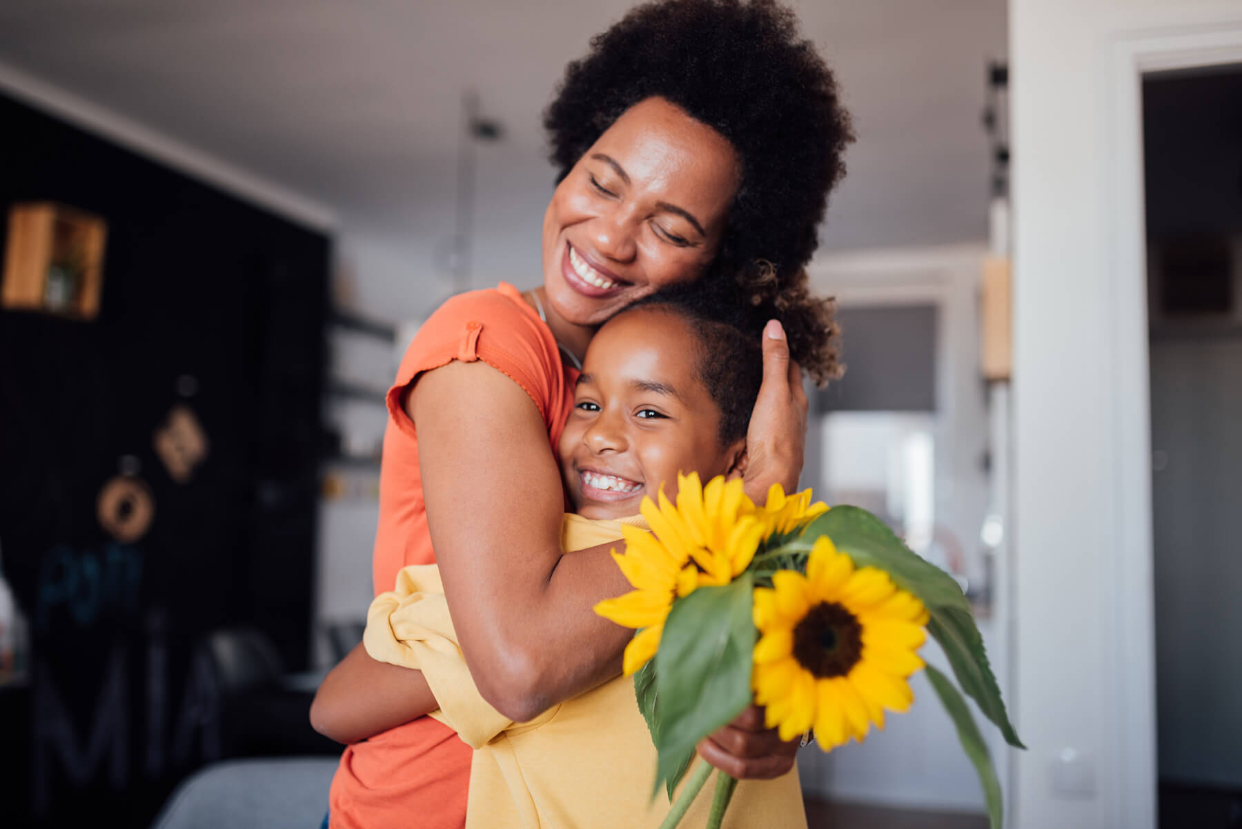 A mother and daughter embrace, holding sunflowers