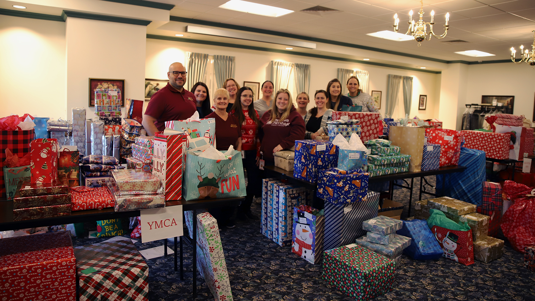 Adopt-A-Family Volunteers stand between tables of wrapped presents.