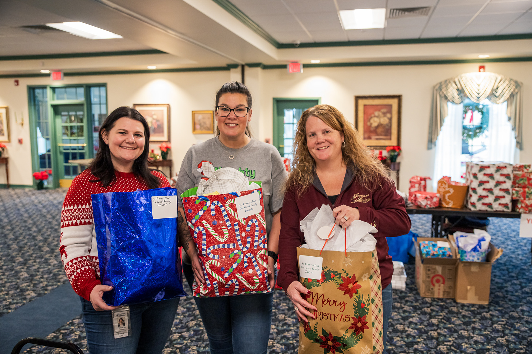 Three volunteers hold wrapped gifts that will be distributed to local families.