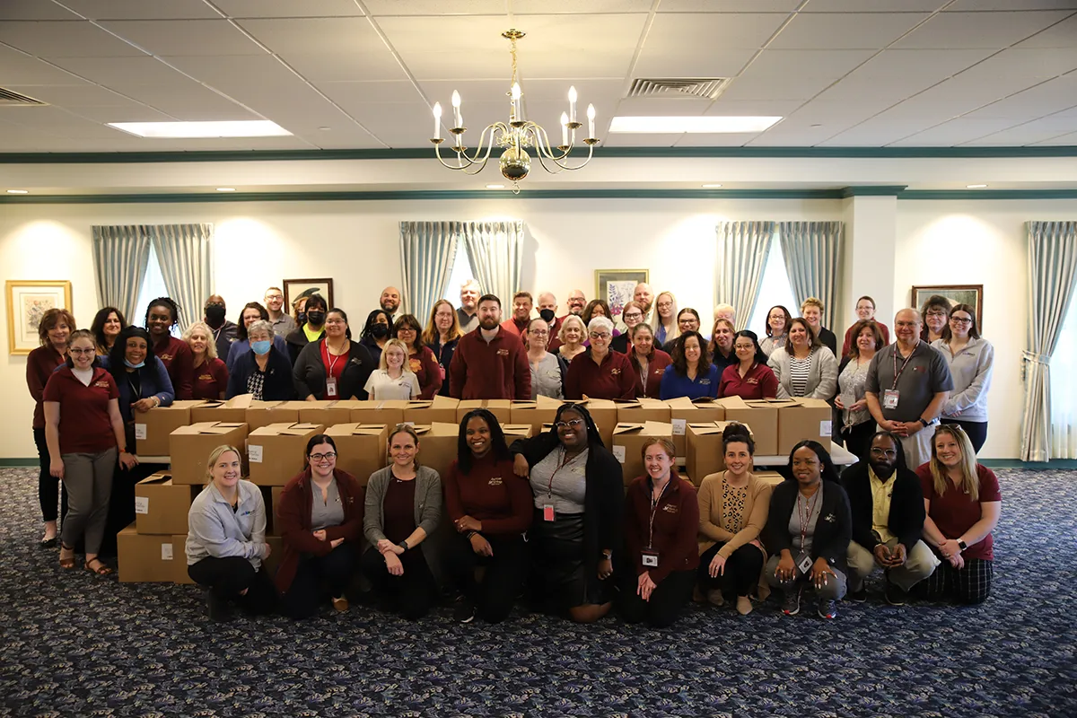 50 American Heritage associates stand and kneel around 50 boxes of packed snack bags.