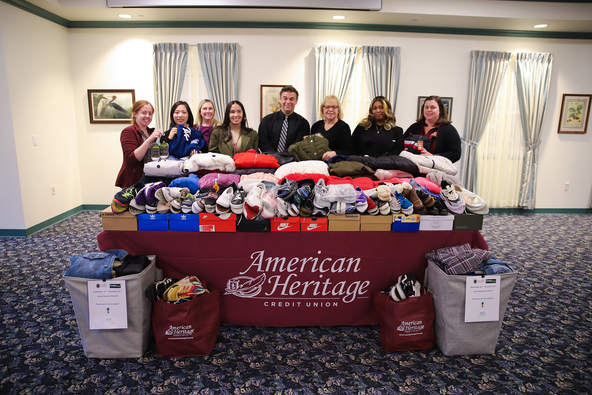 Green Team Committee members stand behind table full of coats and pairs of sneakers.