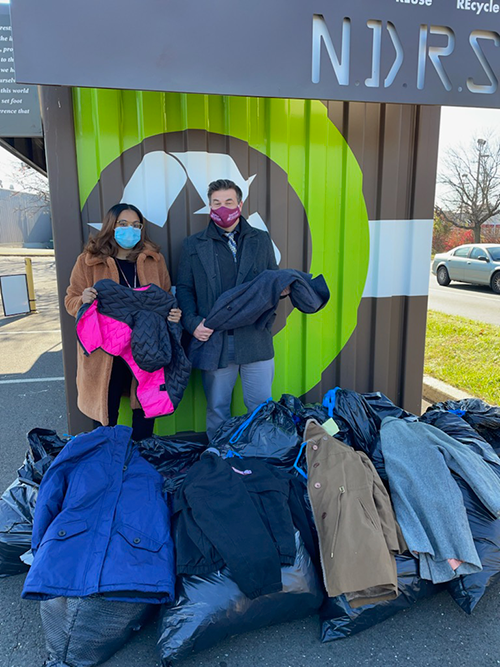 Two coat drive volunteers stand behind bags of donated coats.